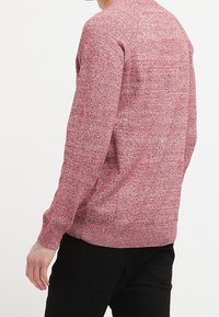 Röd texturerad tröja med rund hals och långa ärmar, med ett subtilt fläckigt mönster, i kombination med svarta byxor.