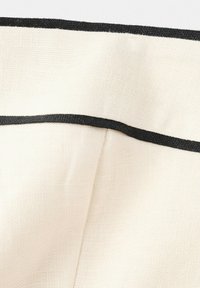 Gros plan d'un tissu blanc texturé avec une bordure horizontale noire et un détail de couture verticale.