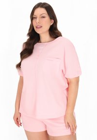 Set de loungewear roz cu mânecă scurtă, prezentând un design texturat, o buzunar pe piept la partea de sus și pantaloni scurți asortați cu o croială lejeră.