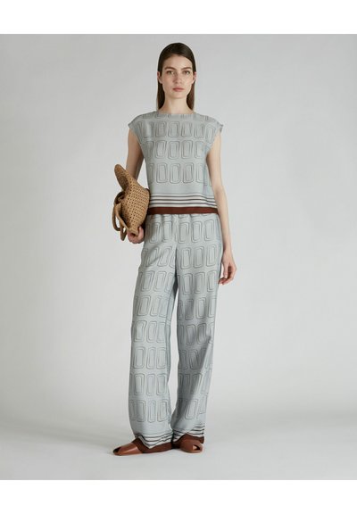 Outfit di un grigio chiaro composto da una blusa a maniche corte con motivo e pantaloni a gamba larga, accentuato da strisce marrone scuro. Inclusa borsa intrecciata.
