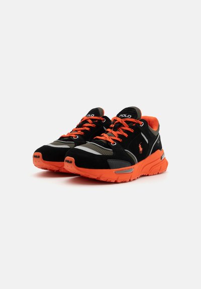 Schwarze und orange Sportschuhe mit einem Obermaterial aus Wildleder und Mesh, orangefarbenen Schnürsenkeln, reflektierenden Details und einer strukturierten Sohle.