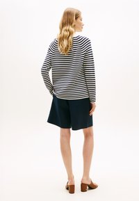 Ριγέ πλεκτό πουλόβερ σε λευκό και ναυτικό μπλε, με μακριά μανίκια. Συνδυασμένο με σορτς μέχρι το γόνατο σε ναυτικό μπλε και καφέ σανδάλια με χοντρό τακούνι.