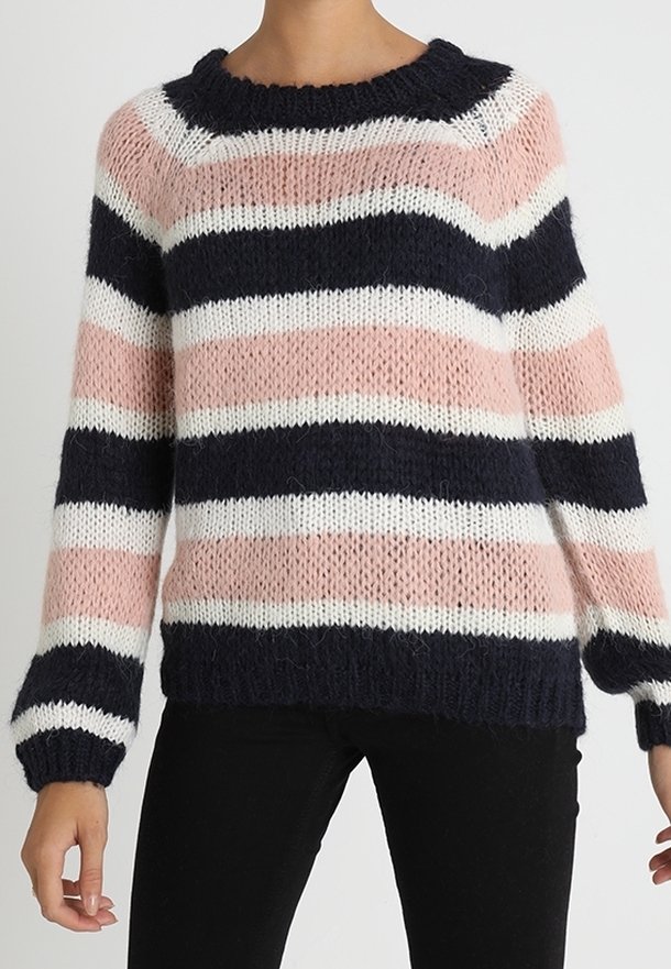 Femme portant un pull en maille ample à rayures horizontales bleu marine, rose et blanc, associé à un pantalon noir.