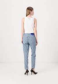 Top blanco sin mangas y jeans azules con un patrón y forma ajustada; zapatos de tacón alto negros; etiqueta de logo visible en los jeans.