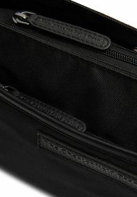 Borsa in tessuto nero con una superficie liscia. Presenta più scomparti con zip e un'etichetta in pelle goffrata con il marchio.