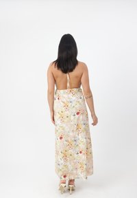 Robe maxi florale dans des couleurs pastel, avec un dos ouvert, des bretelles spaghetti et une silhouette fluide. Tissu doux avec une texture légère.