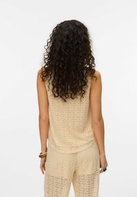 Beige gehaakte tanktop, mouwloos met een relaxed fit. Kenmerkt zich door een ingewikkeld patroon en wordt gecombineerd met bijpassende losse broek.