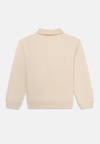 Polo beige à manches longues avec col, poignets et ourlet côtelés. Texture lisse avec un motif tissé subtil sur le tissu.