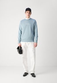 Gaiši zils džemperis, zem tā balta krekls, baltas bikses, melni apavi, melna soma un melna cepure ar logo. Ikdienas apģērbs ar vienkāršu dizainu.