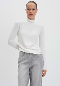 Langärmliges weißes Rollkragenoberteil aus weichem Stoff, kombiniert mit hellgrauen Jeans; hat einen lässigen Schnitt und eine glatte Textur.