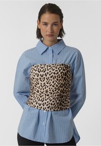 Mėlynas raiščių marškinėliai su raukinėtu leopardų rašto liemeniu. Marškiniai turi ilgomis rankovėmis ir klasikinį apykaklę, pasižymi laisvu siluetu.