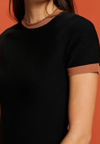 Svart stickad topp med korta ärmar och en kontrasterande brun strukturerad krage. Har en figurnära design och en slät textur.