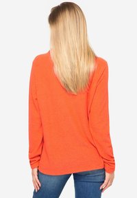 Langarm, feloranje t-shirt van lichtgewicht stof, comfortabele pasvorm, afgeronde zoom en oprolbare mouwdetails. Gecombineerd met blauwe jeans.