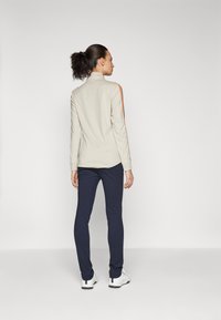 Beige lång�ärmad topp med orange ränder på ärmarna, tillsammans med mörkblå byxor. Outfitten har en hög krage och en figursydd design.
