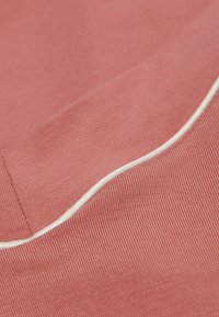 Koralikowy materiał żeberkowy o teksturowej powierzchni, z białą lamówką wzdłuż szwu. Zbliżenie ukazujące detale materiału.