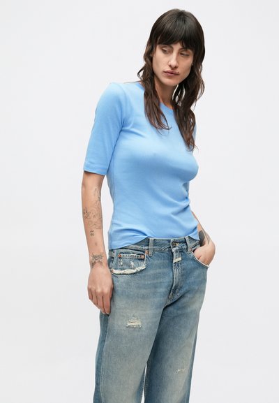 Camicia azzurro chiaro a maniche corte dal taglio aderente abbinata a jeans blu strappati. La camicia ha una texture liscia e un collo classico.
