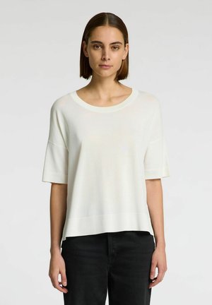 Camiseta de punto blanca con mangas cortas y escote redondo, con dobladillo recto. Combinada con pantalones negros, mostrando un ajuste casual.