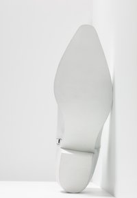 Zapato de tacón alto blanco con parte superior sintética suave y suela de goma texturizada. Diseño notable de punta afilada y tacón esbelto.