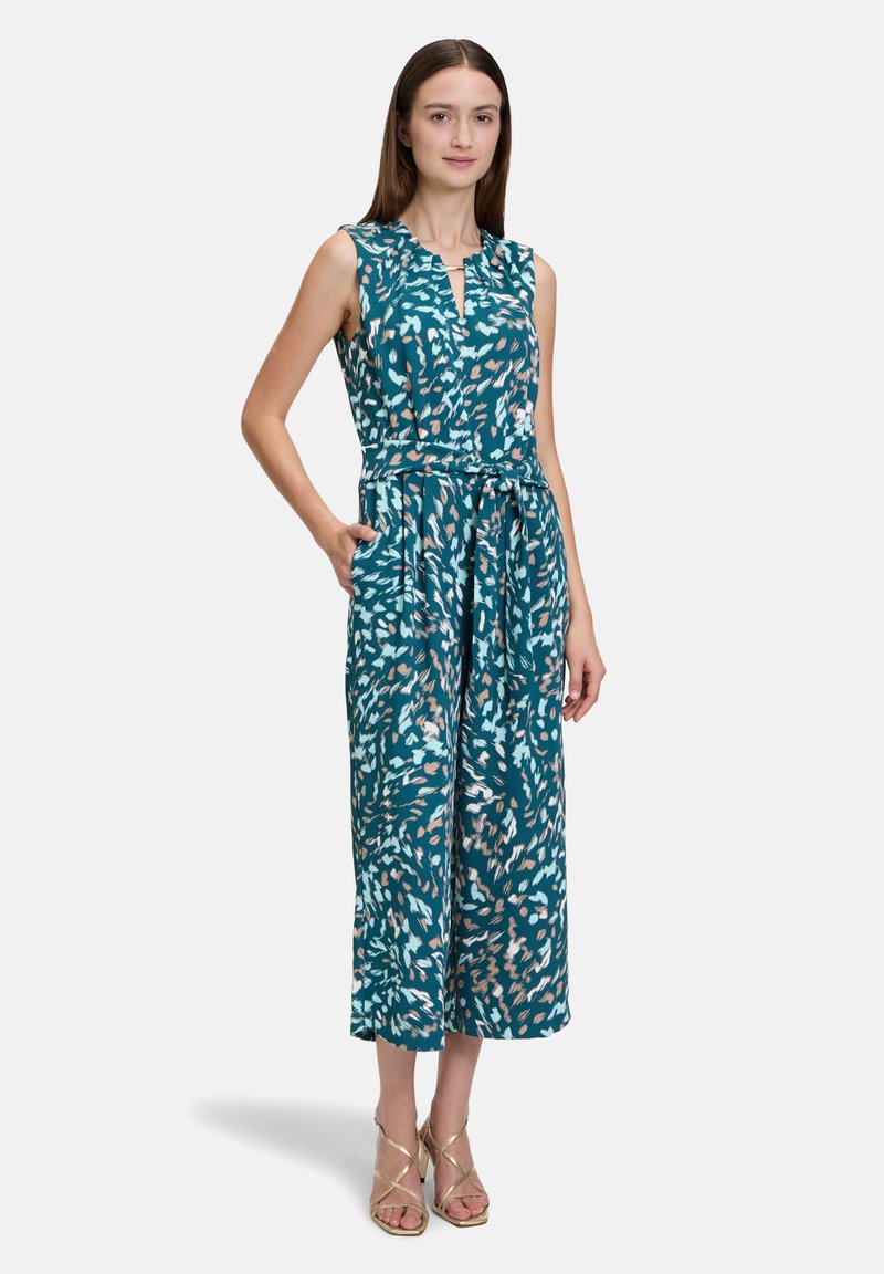 Teal színű, virágmintás ujjatlan kombiné, kulcslyuk fazonú nyakkivágással, megkötős derékkal és széles lábakkal. Könnyű anyag, zsebekkel.