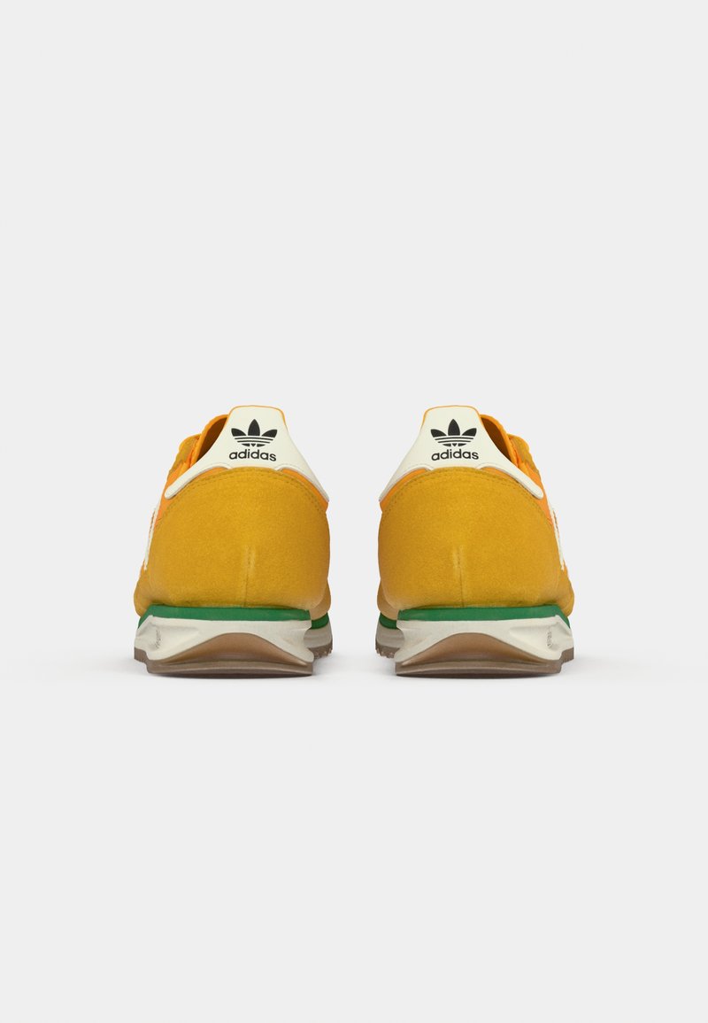 Un par de zapatillas Adidas en naranja y amarillo vistas desde atrás, con pestañas blancas en el talón que llevan el logo negro de Adidas y mediasuelas verdes.
