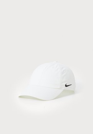 Căciulă de baseball din bumbac alb, cu o visor curbată, având un logo Nike negru pe lateral și detalii de cusătură vizibile.