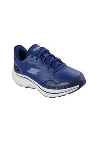 Zapato deportivo azul con parte superior de malla texturizada, puntera redondeada y suela blanca moteada. Presenta cordones planos y un logotipo en la lengüeta.