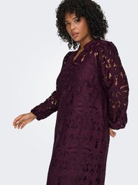 Lång, djupt lila spetsklänning med blommönster och intrikata utskärningar. Den har en V-ringning och långa, rynkade ärmar.