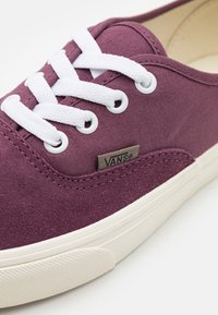 Detailní záběr na fialovou tenisku Vans s bílými tkaničkami, bílou gumovou podrážkou a malou visačkou s logem Vans na boku.