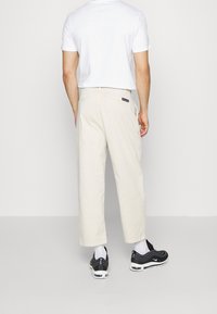 Beige cargobyxor med avslappnad passform, med sidofickor och ett märke på baksidan. Kombinerade med svarta sneakers och vita strumpor.