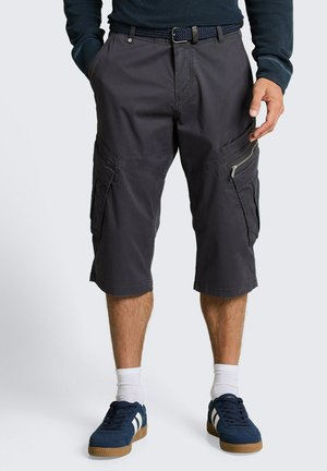 Mann trägt dunkelgraue Cargoshorts mit Reißverschlusstaschen, geflochtenem Gürtel, weißen Socken und dunkelblauen Sneakers mit weißen Streifen.