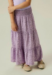 Falda morada de flores con volantes y cintura fruncida. Tejido ligero con detalles de dobladillo con volante. Combinada con zapatos beige con hebilla.