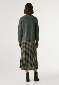 Suéter cinza de malha com bainha canelada, combinado com uma saia midi xadrez preta e botas de tornozelo pretas. Textura suave e corte relaxado.