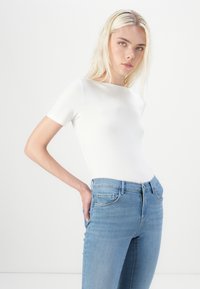 Bijela prsluk kratkih rukava u kombinaciji s svijetloplavim trapericama, s običnim džepovima i elegantnom, glatkom teksturom tkanine.