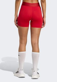 Red athletic shorts made of stretchy fabric with a high waistband. Paired with white knee-length socks and black-and-white sneakers.
