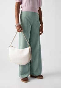 Borsa a spalla bianca in pelle con una forma curva, dotata di una tracolla corta, hardware in oro e una finitura testurizzata. Indossata con pantaloni in corduroy verde menta.