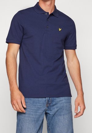 Marineblå polo lavet af bomuld med en tre-knaps placket og en broderet gul logo på venstre bryst. Korte ærmer.