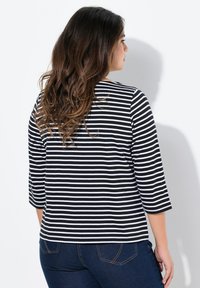 Musta-valkoiset raidalliset pitkähihainen paita, jossa on pyöreä pääntie, rento mallisto ja pehmeä kangas, yhdistettynä tummansinisiin farkkuihin.