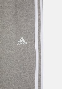 Gray sweatpants made of soft fabric, featuring white side stripes and an embroidered white Adidas logo on the left thigh.