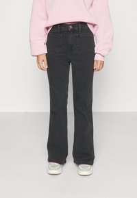 Sorte utsvingte jeans med høy livde, to frontlommer og minimale sømdetaljer, kombinert med hvite og fargerike sneakers.