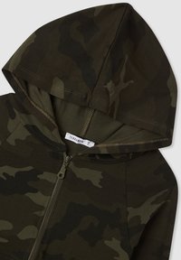 Felpa con zip mimetica in tonalità di verde scuro e marrone, dotata di cappuccio, tessuto morbido e cuciture rinforzate lungo la zip.