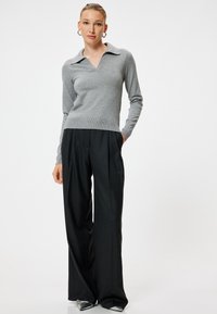 Grijze, lange mouwen pullover met een V-hals en kraag, gecombineerd met zwarte, wijde broek en zilveren puntige schoenen. Glad textuur.