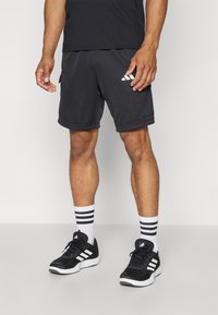 Black athletic shorts with side pockets, grey fabric, curved hem, and white Adidas logo. Paired with striped white and black socks and black shoes.
