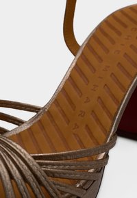 Καφέ σανδάλι με λουριά και υφασμένη εσωτερική σόλα με ριγέ μοτίβο και μερικώς ορατό κείμενο σε λευκό φόντο.