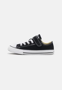 Fekete vászon sneaker fehér fűzővel és gumitippel. Jellemzi egy pánt a nyelv felett és fehér oldalfal fekete csíkokkal.