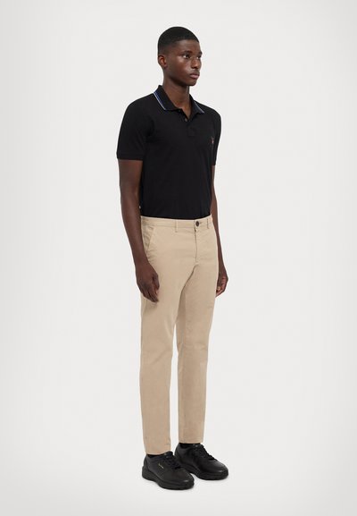 Camisa polo negra con cuello en contraste, chinos beige y zapatillas negras. Corte casual; textura acanalada en el cuello y tejido suave en los pantalones.