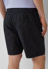 Zwarte shorts met een elastische tailleband, zijkleppen en een enkele achterzak. Het materiaal lijkt licht en ademend te zijn.