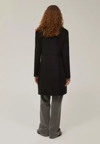 Cappotto nero con una vestibilità su misura, maniche lunghe e taglio di media lunghezza. Caratterizzato da un design semplice senza motivi o accessori visibili.