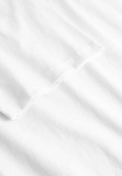 Nærbilde av et hvitt stoff som viser en sydd kant med fine sømmer på en glatt overflate.