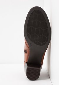 Bottine en cuir marron à finition lisse, dotée d'une semelle en caoutchouc noire avec un motif de bande de roulement hexagonal et un détail de fermeture éclair latérale.