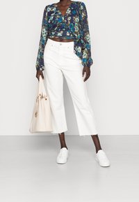 Blouse cache-cœur fleurie à manches longues en bleu, vert et blanc ; associée à un jean large blanc raccourci ; accessoirisée d'un sac à main beige et de baskets blanches.